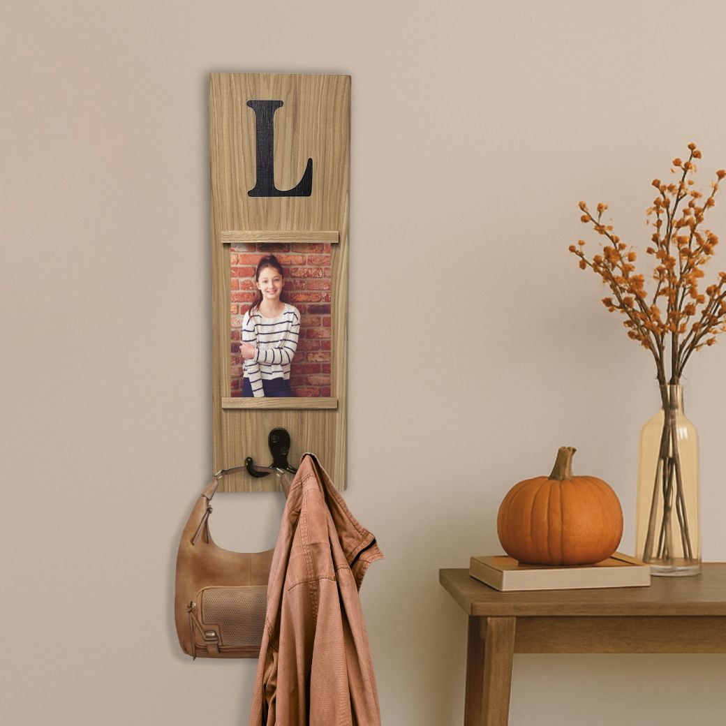 Wooden wall hook with a photo frame and coat, pumpkin, and vase on a table against a beige wall.