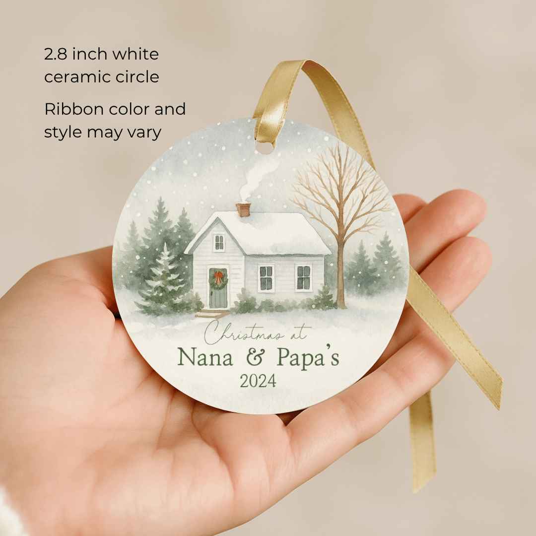 Decorative Christmas ornament with a house and trees, held by a hand against a beige background.