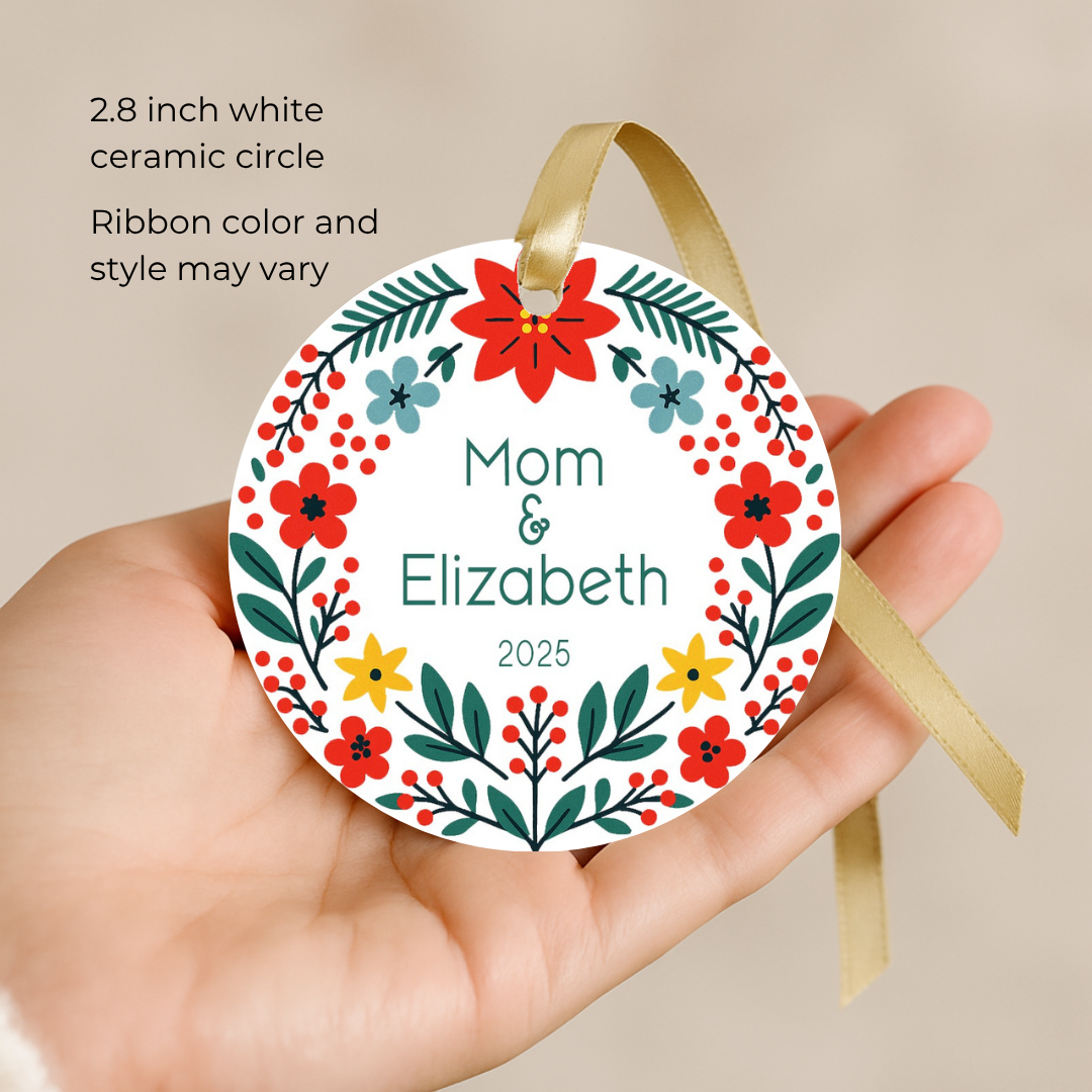 Round ceramic personalized Christmas ornament with floral design held in a hand, against a beige background.