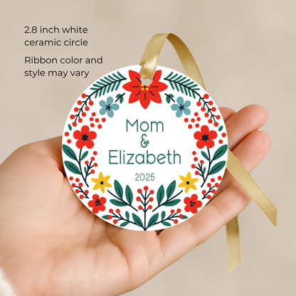 Round ceramic personalized Christmas ornament with floral design held in a hand, against a beige background.