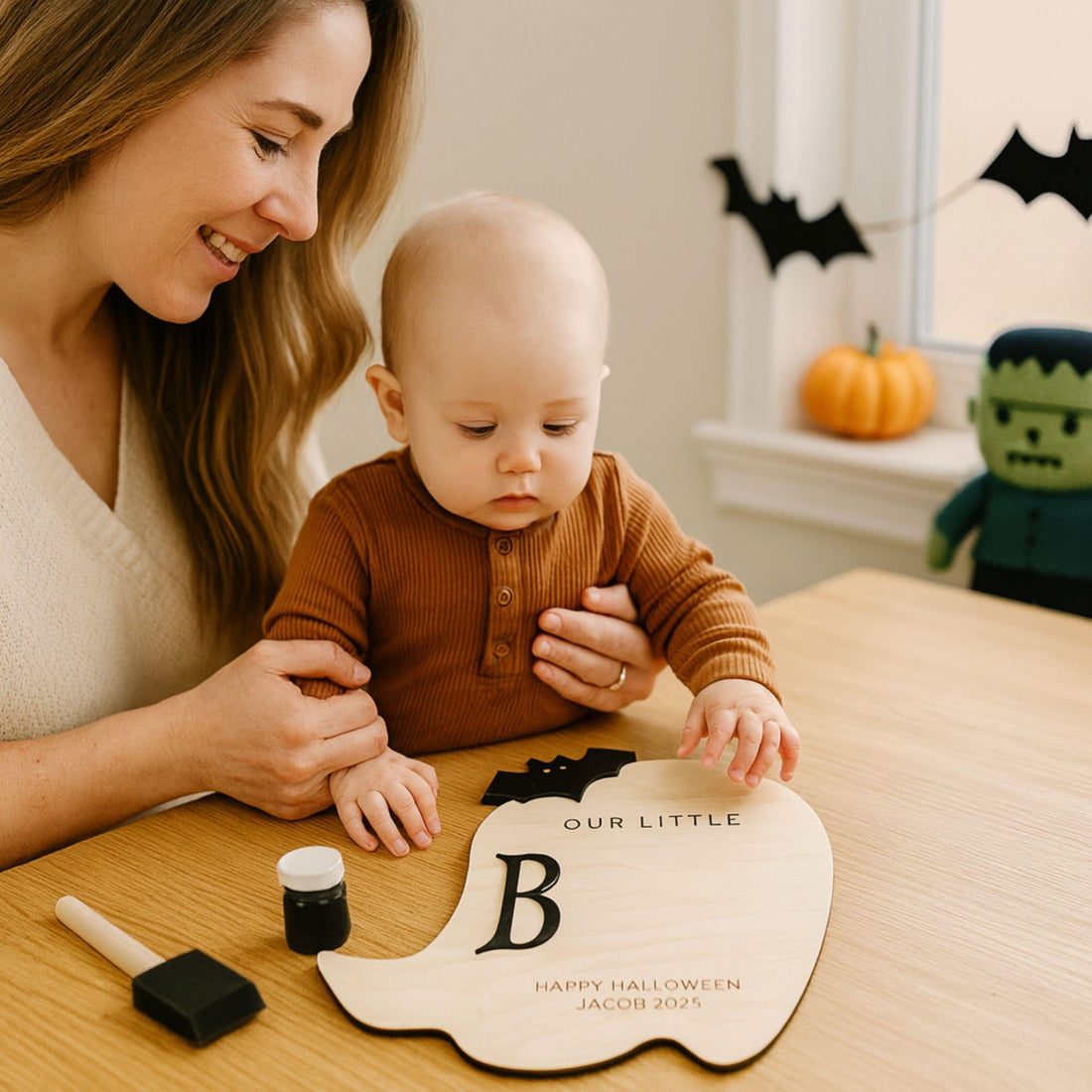 Woman and baby with a Halloween-themed footprint or handprint craft project on a table.