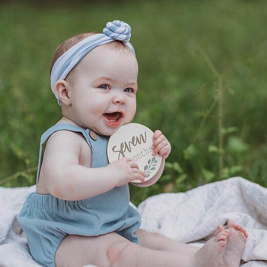 Baby girl in blue holding 7 month botanical baby milestone card