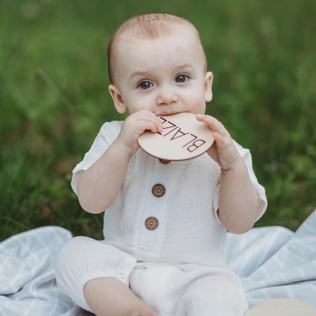 Baby boy in white romper holding woodeb name card