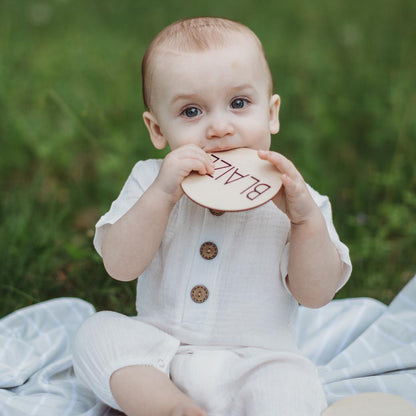 Baby boy in white romper holding woodeb name card