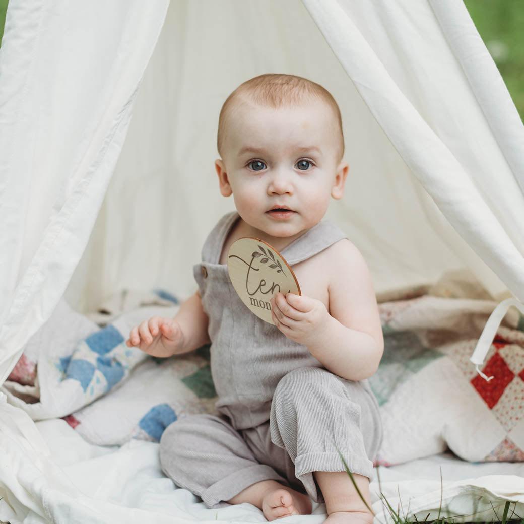 Baby boy holding olive milestone cards at 10 months