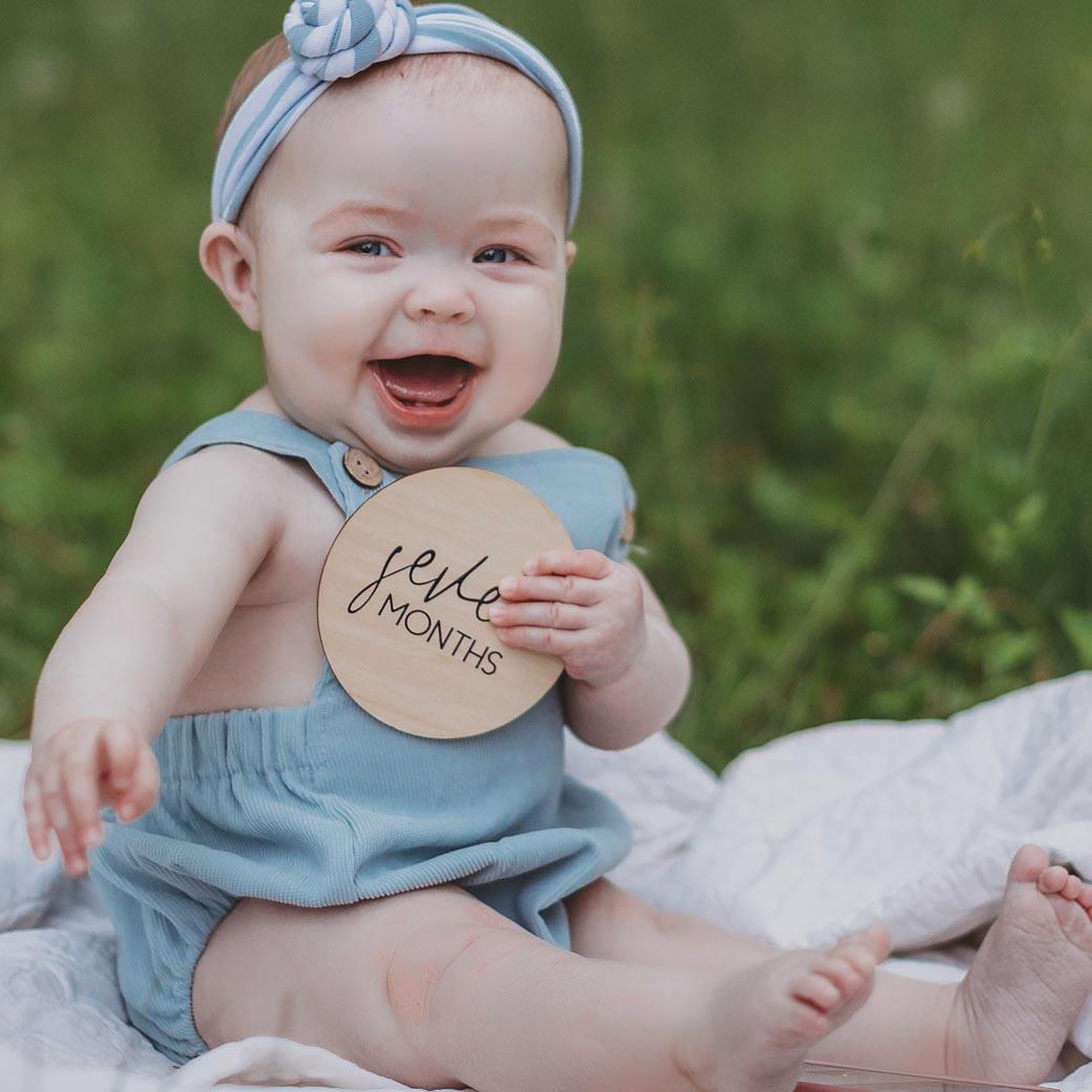 Smiling baby holding 7 month milestone card