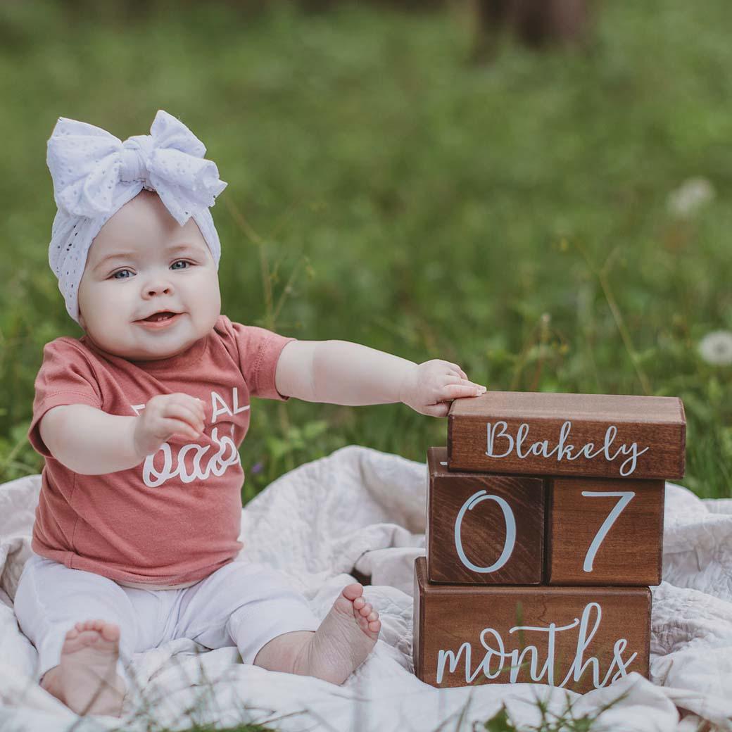 Baby touching her name block with Willow milestone blocks at 07 months