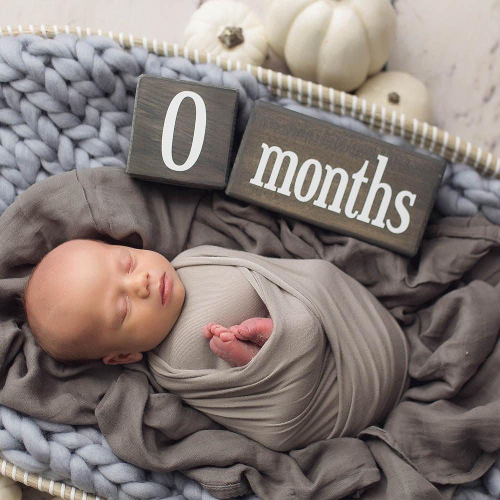 Sleeping newborn with Hickory baby milestone blocks in dark gray at 0 months