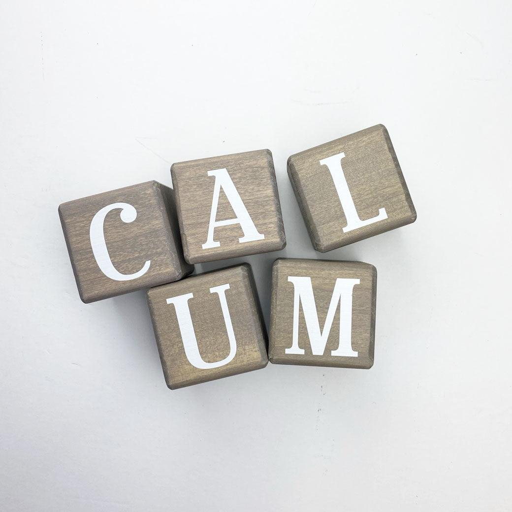 Wooden letter blocks in sand spelling Calum